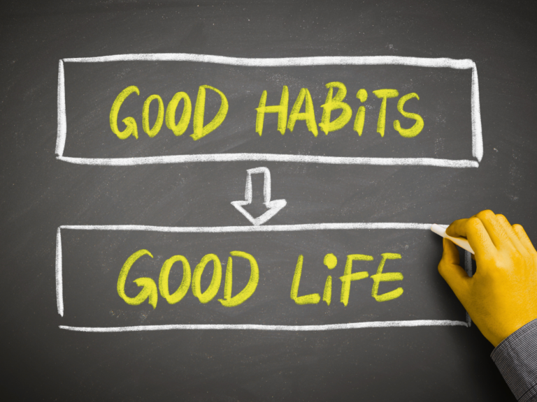 Hand writing “Good Life” beneath “Good Habits” on a chalkboard, illustrating how positive daily habits can lead to a better life.